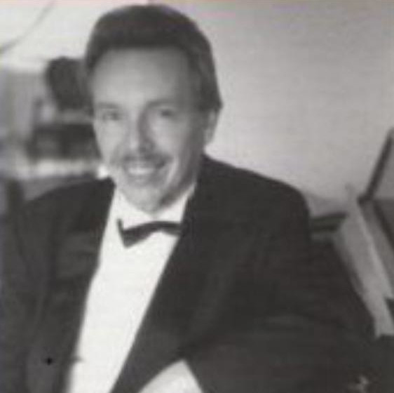 A black-and-white photo of a man in a tuxedo, smiling