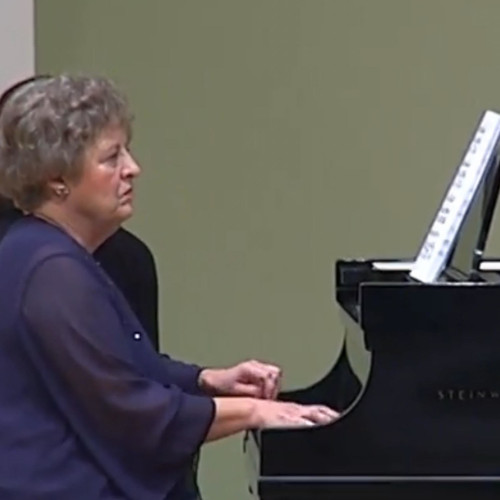 A woman with grey curly hair, playing the piano