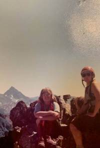 Two people atop a mountain, wearing climbing gear